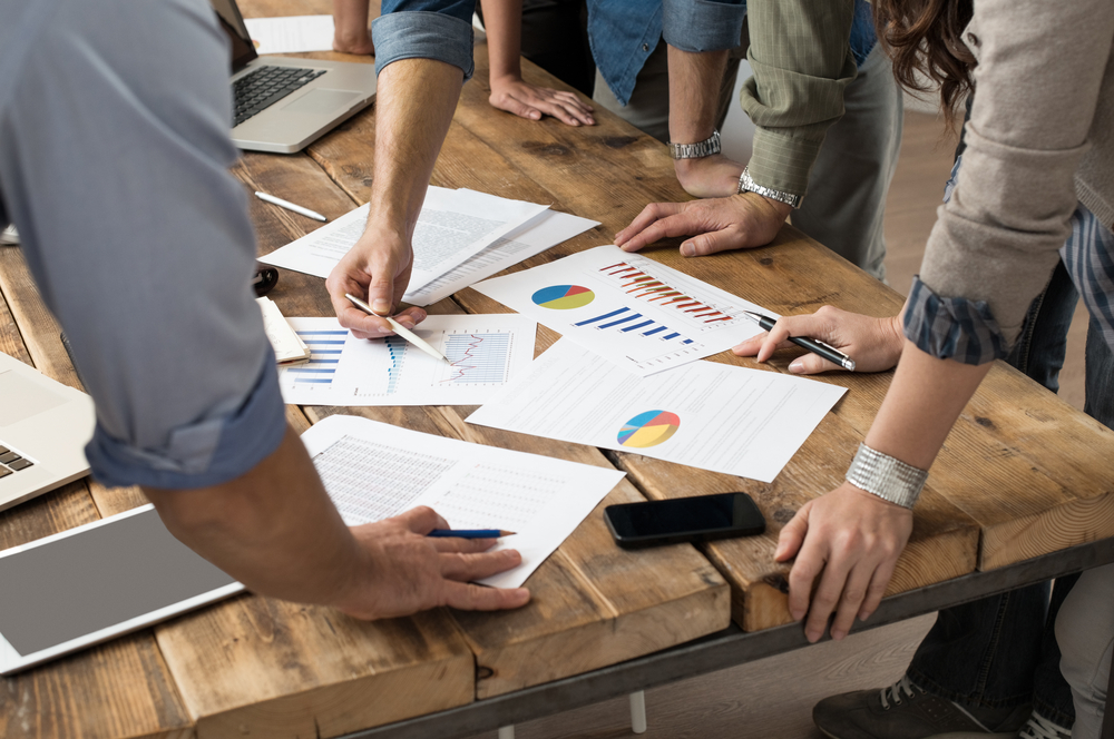 Businessman,And,Woman,Discussing,On,Stockmarket,Charts,In,Office